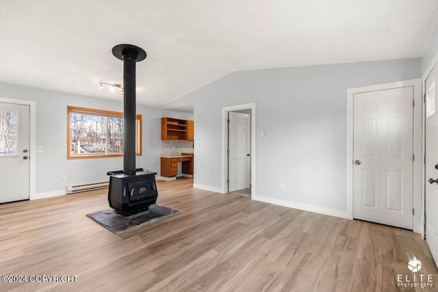 unfurnished living room with lofted ceiling, baseboards, baseboard heating, light wood finished floors, and a wood stove