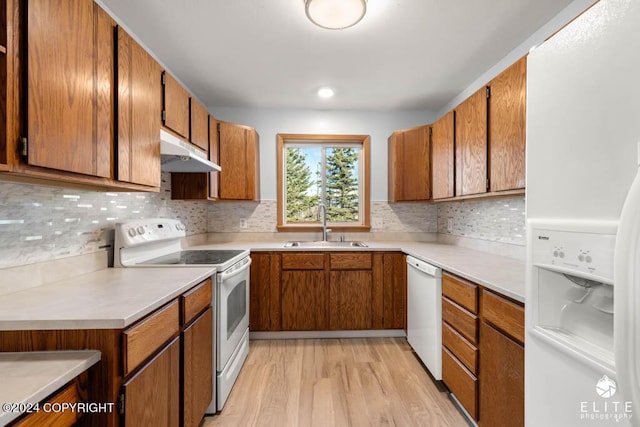 kitchen with under cabinet range hood, white appliances, a sink, light countertops, and brown cabinetry