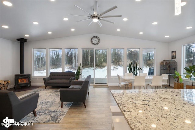 living area with lofted ceiling, a healthy amount of sunlight, light wood-style flooring, and a wood stove