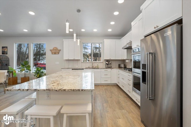 kitchen featuring stainless steel appliances, light wood-style flooring, white cabinetry, a kitchen island, and under cabinet range hood