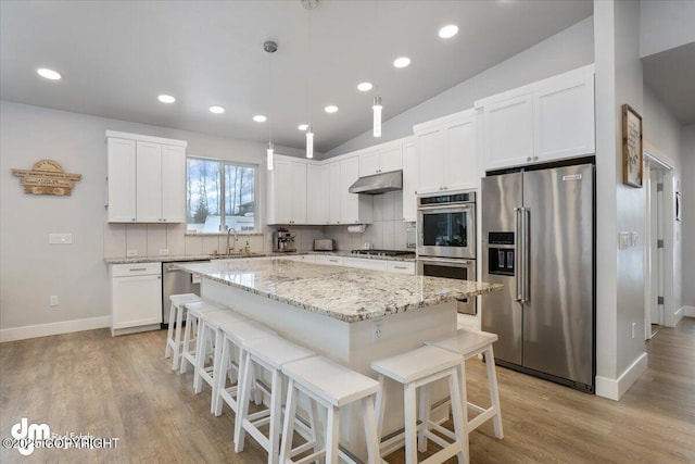 kitchen featuring backsplash, appliances with stainless steel finishes, white cabinetry, a kitchen island, and under cabinet range hood