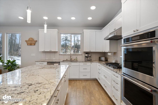 kitchen with under cabinet range hood, appliances with stainless steel finishes, backsplash, and a sink