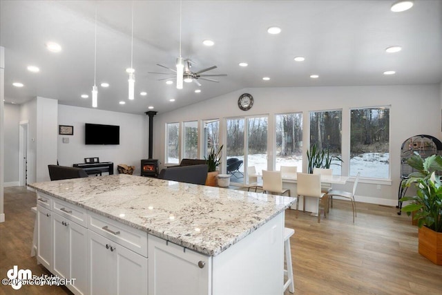 kitchen with a center island, a wood stove, white cabinetry, vaulted ceiling, and wood finished floors