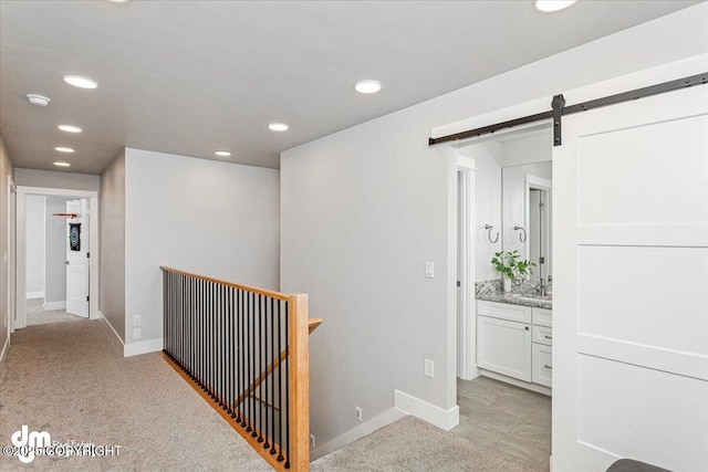 hallway with a barn door, baseboards, a sink, and recessed lighting