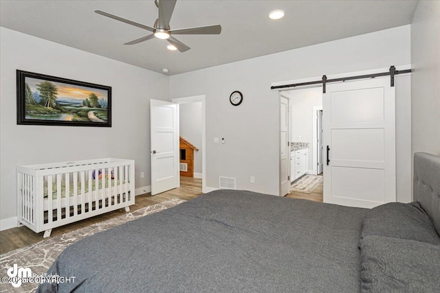 bedroom with a barn door, baseboards, visible vents, wood finished floors, and recessed lighting