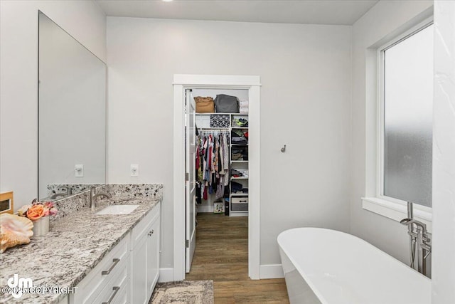 bathroom featuring a walk in closet, vanity, wood finished floors, a freestanding tub, and baseboards