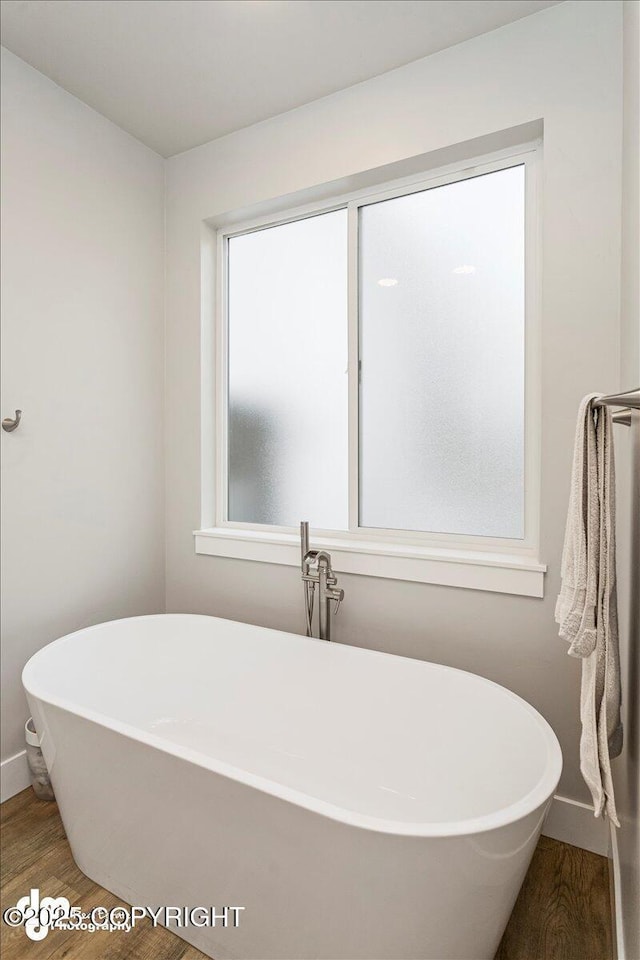 bathroom with a soaking tub, wood finished floors, and baseboards