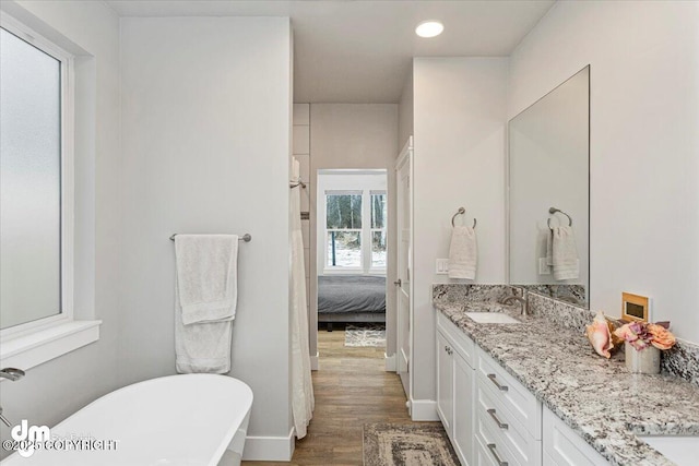 ensuite bathroom featuring double vanity, a freestanding bath, a sink, wood finished floors, and baseboards