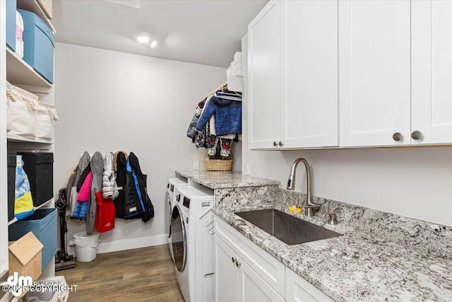 clothes washing area with cabinet space, a sink, separate washer and dryer, wood finished floors, and baseboards