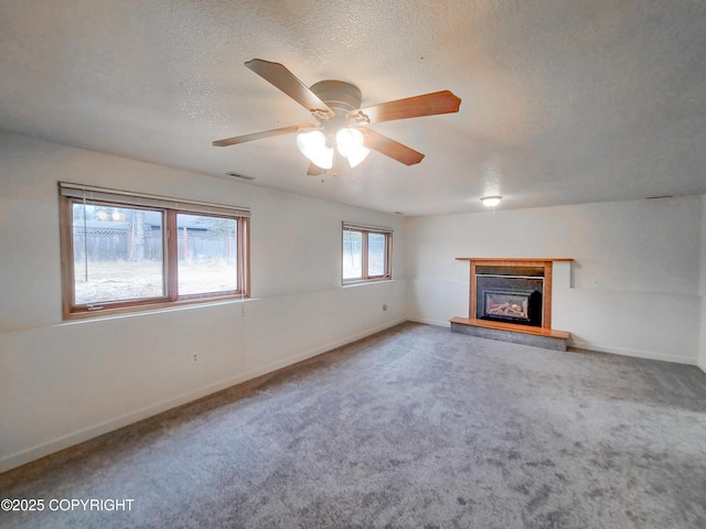 unfurnished living room with carpet, visible vents, a glass covered fireplace, a textured ceiling, and baseboards