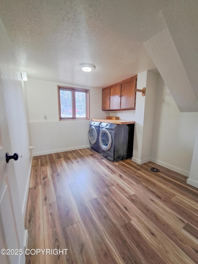 washroom with cabinet space, baseboards, wood finished floors, a textured ceiling, and separate washer and dryer