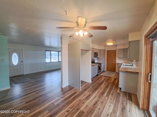 kitchen featuring appliances with stainless steel finishes, open floor plan, a sink, a textured ceiling, and wood finished floors