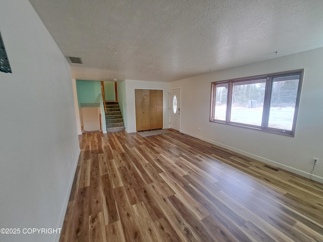 unfurnished living room with a textured ceiling, stairs, visible vents, and wood finished floors