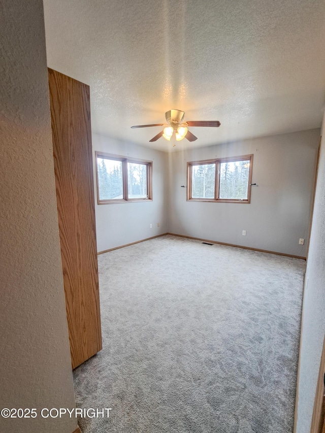 spare room featuring visible vents, a textured ceiling, carpet flooring, and a wealth of natural light