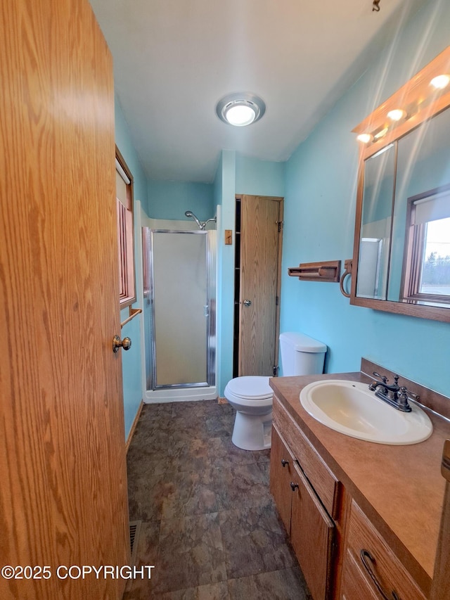 full bath featuring stone finish floor, a shower stall, toilet, and vanity