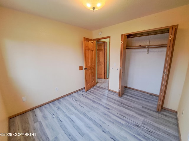 unfurnished bedroom featuring a closet, light wood-style flooring, and baseboards