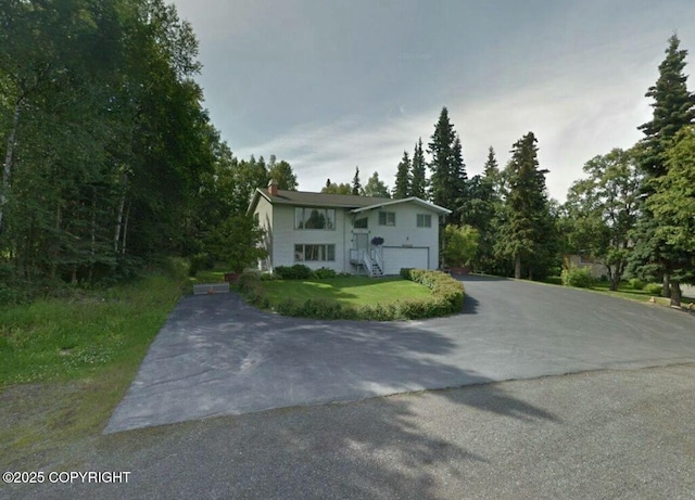 bi-level home featuring a garage, aphalt driveway, and a front yard