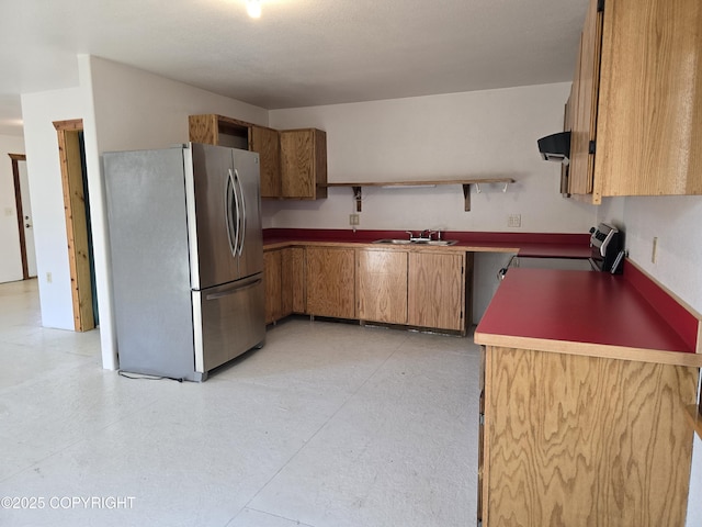 kitchen featuring open shelves, stove, brown cabinetry, freestanding refrigerator, and ventilation hood