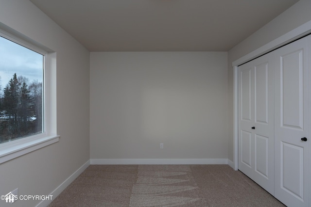 unfurnished bedroom featuring baseboards, a closet, and light colored carpet