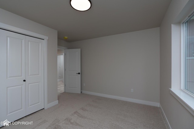 unfurnished bedroom featuring light carpet, baseboards, and a closet