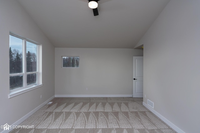 spare room featuring a ceiling fan, visible vents, vaulted ceiling, baseboards, and carpet