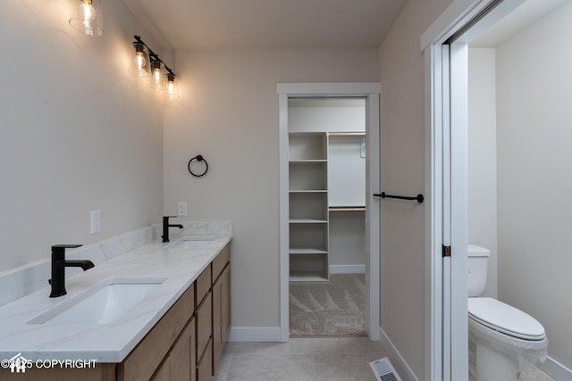 bathroom featuring toilet, visible vents, a walk in closet, and a sink