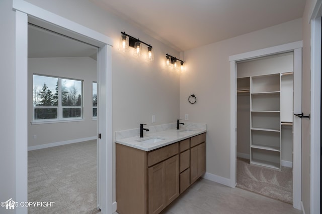 bathroom featuring a spacious closet, double vanity, a sink, and baseboards