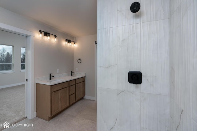 full bathroom featuring a sink, a tile shower, baseboards, and double vanity