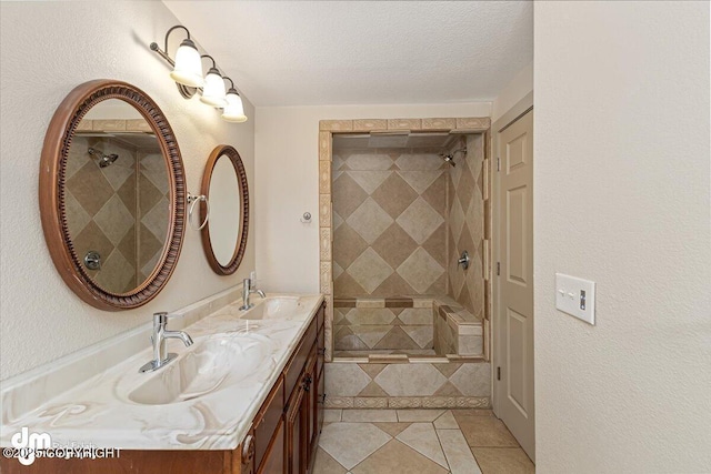 full bath with a sink, a textured ceiling, double vanity, and a tile shower