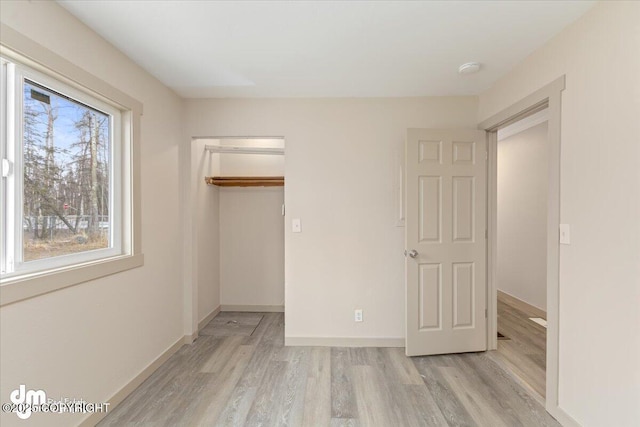 unfurnished bedroom with a spacious closet, baseboards, light wood-type flooring, and a closet