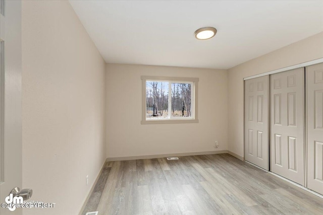 unfurnished bedroom featuring light wood finished floors, a closet, and baseboards