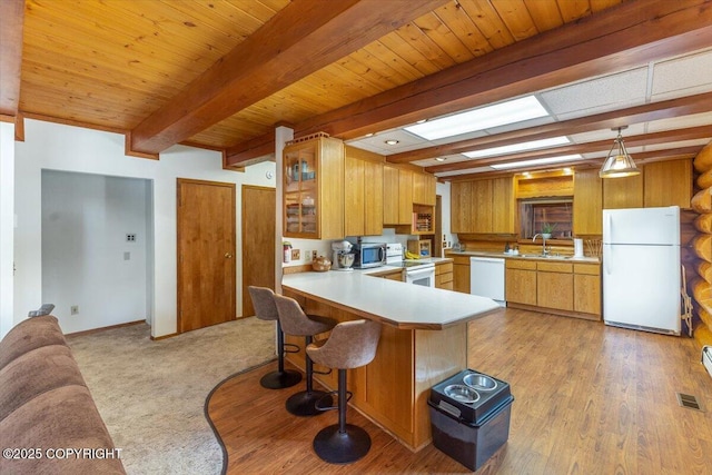 kitchen featuring a peninsula, white appliances, a sink, light countertops, and beamed ceiling