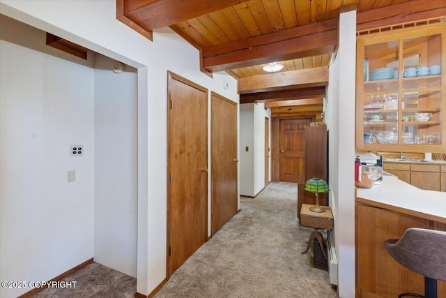 corridor featuring wood ceiling, beam ceiling, light colored carpet, and baseboards