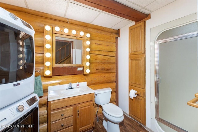 bathroom with toilet, a paneled ceiling, vanity, an enclosed shower, and stacked washer and clothes dryer