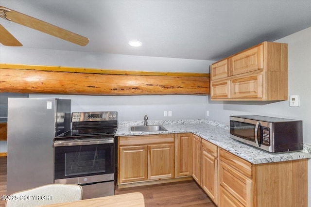 kitchen with appliances with stainless steel finishes, wood finished floors, light stone countertops, light brown cabinets, and a sink