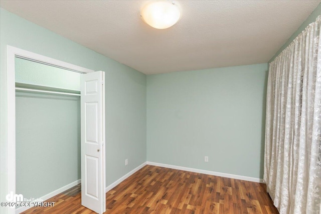 unfurnished bedroom featuring a closet, a textured ceiling, baseboards, and wood finished floors