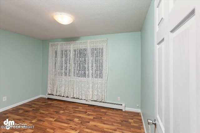 empty room with a textured ceiling, a baseboard radiator, wood finished floors, and baseboards