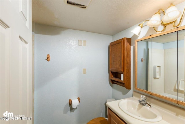 bathroom with a textured ceiling, vanity, and visible vents