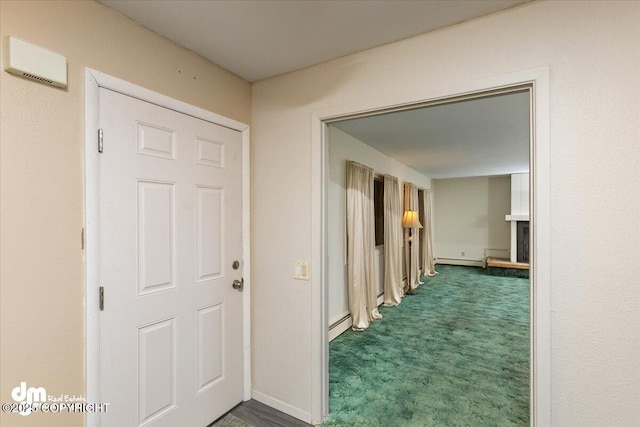 corridor featuring dark colored carpet, baseboard heating, and baseboards