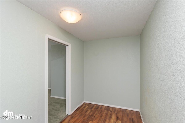 empty room featuring a textured wall, dark wood finished floors, a textured ceiling, and baseboards