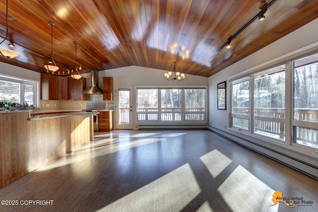 kitchen with wall chimney exhaust hood, a notable chandelier, lofted ceiling, brown cabinets, and track lighting