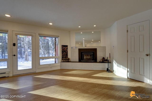 unfurnished living room with recessed lighting, a healthy amount of sunlight, wood finished floors, and a tiled fireplace