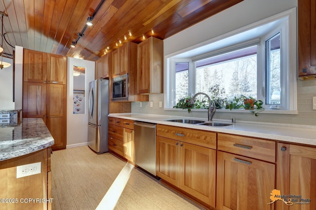 kitchen with a sink, brown cabinets, decorative backsplash, rail lighting, and appliances with stainless steel finishes