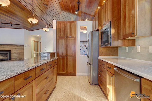 kitchen with tasteful backsplash, a stone fireplace, hanging light fixtures, brown cabinetry, and stainless steel appliances