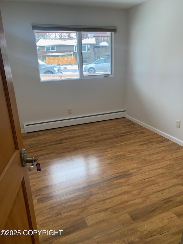 unfurnished room with a baseboard heating unit, wood finished floors, and baseboards