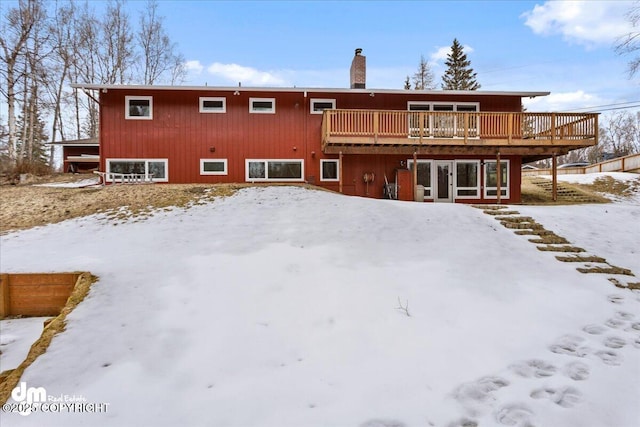snow covered house featuring a wooden deck and a chimney
