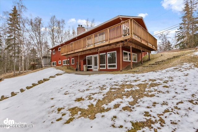 snow covered back of property featuring a wooden deck and a chimney