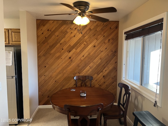 dining area featuring light carpet, baseboards, a ceiling fan, and wooden walls