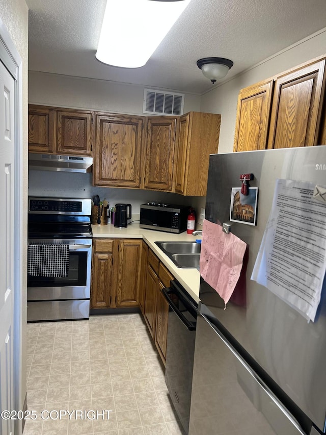 kitchen with under cabinet range hood, a sink, visible vents, appliances with stainless steel finishes, and brown cabinets