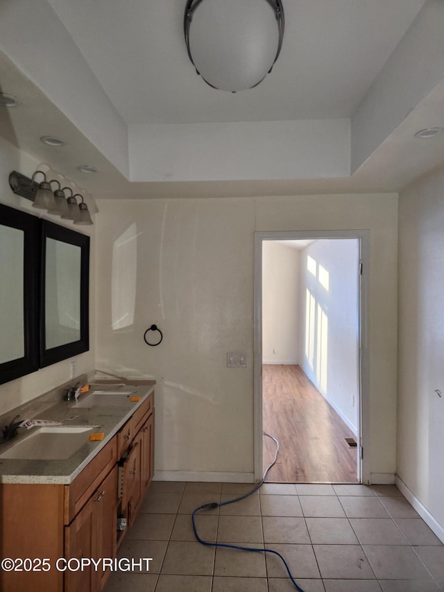 bathroom featuring baseboards, double vanity, a sink, and tile patterned floors